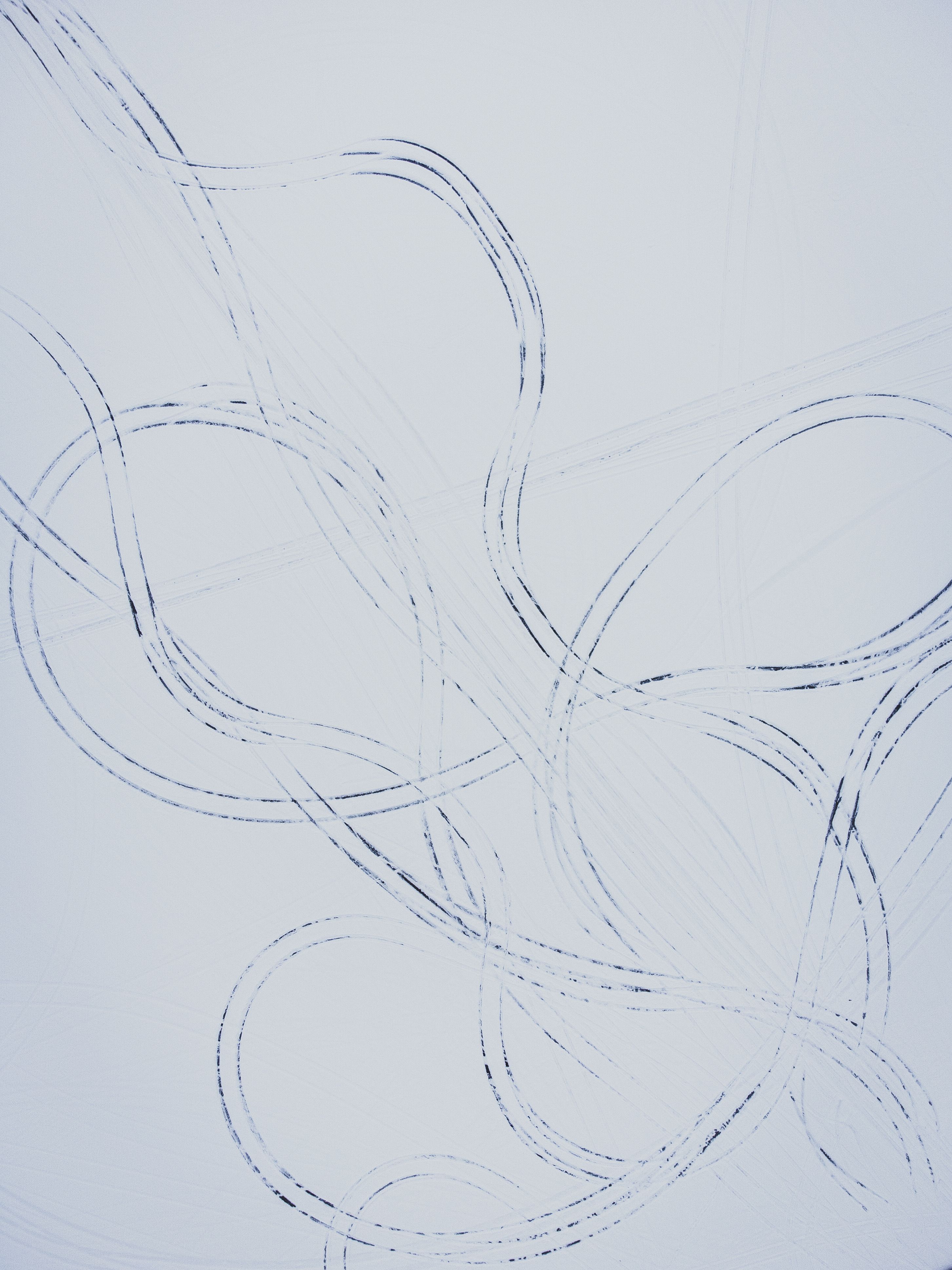 Artistic abstract pattern created by car tracks in the snow, showing intricate loops and curves.