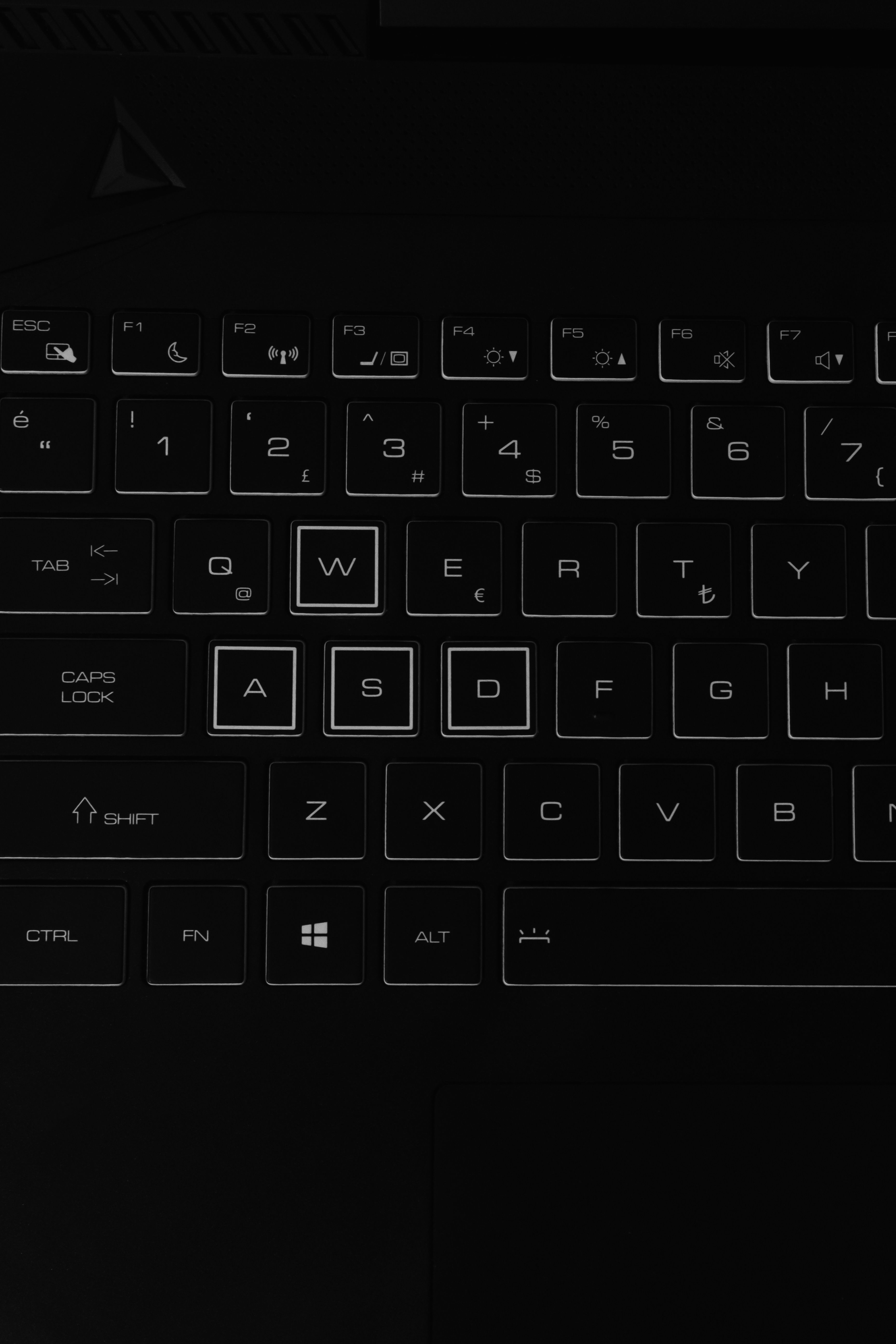 Close-up of a laptop keyboard with illuminated keys in a dark setting, highlighting key details.