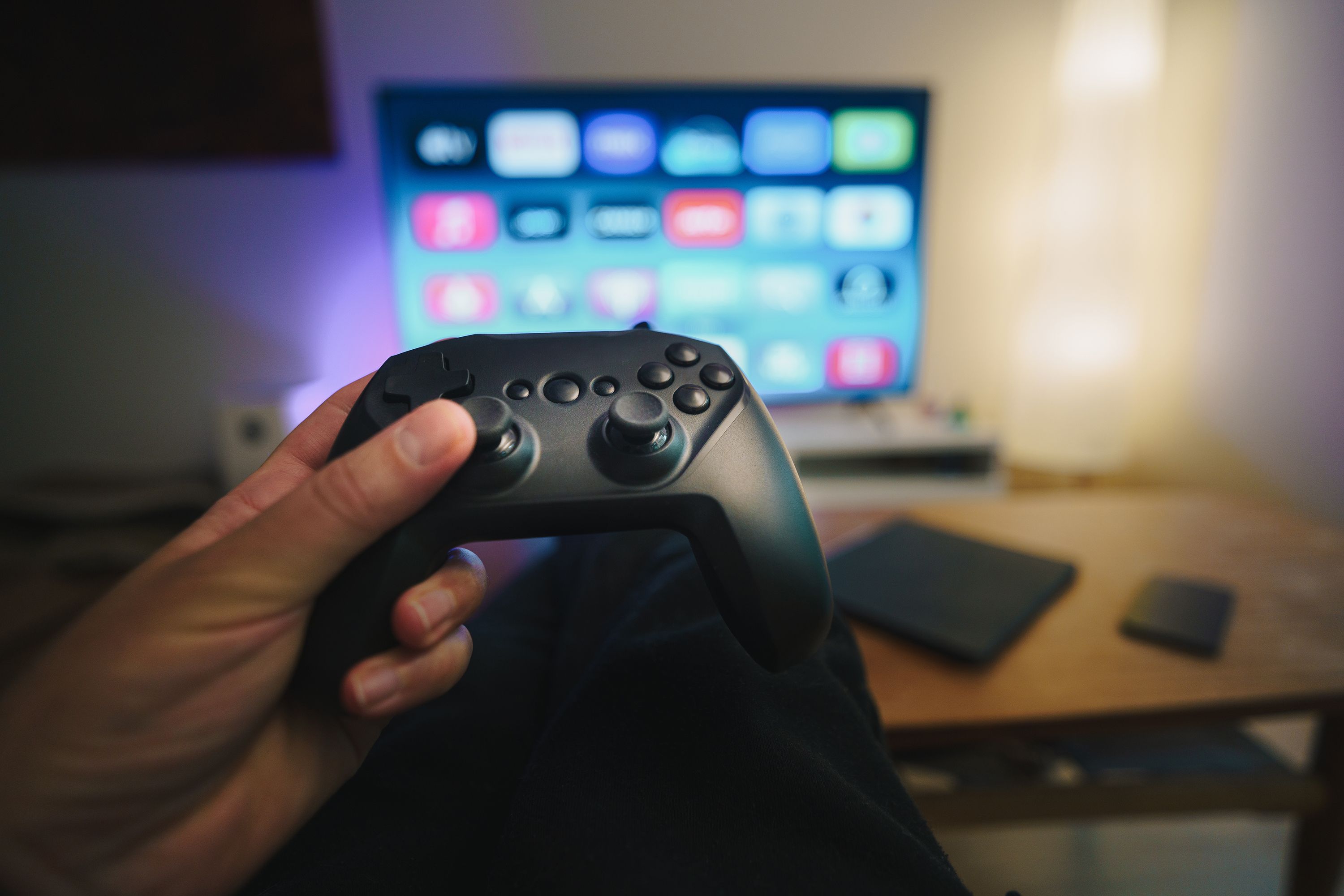Close-up of a person holding a gaming controller in a cozy living room setup with TV.