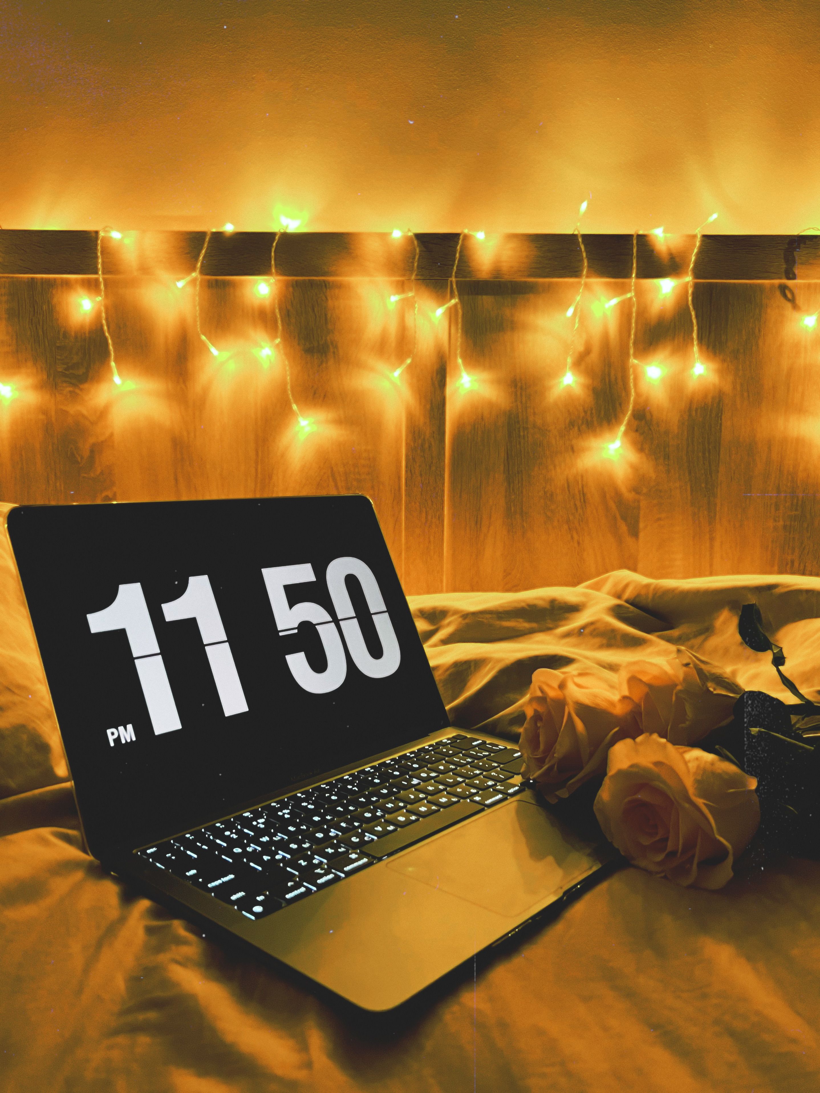 Warm cozy scene with a laptop and fairy lights at 11:50 PM in a bedroom setting. Ideal for relaxation themes.