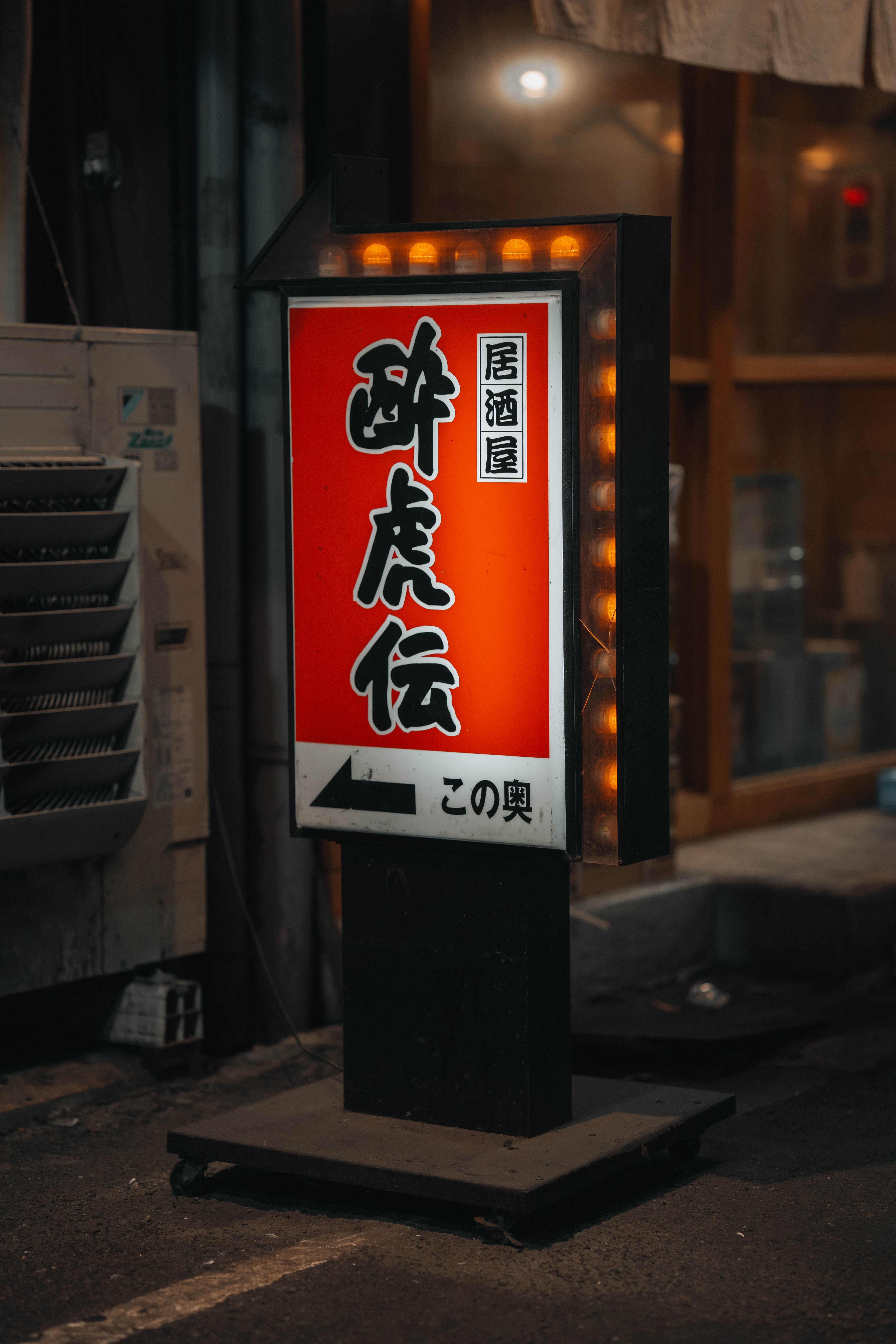 Capture of an illuminated izakaya sign glowing in a dark Japanese street,  evoking a vibrant nightlife scene.