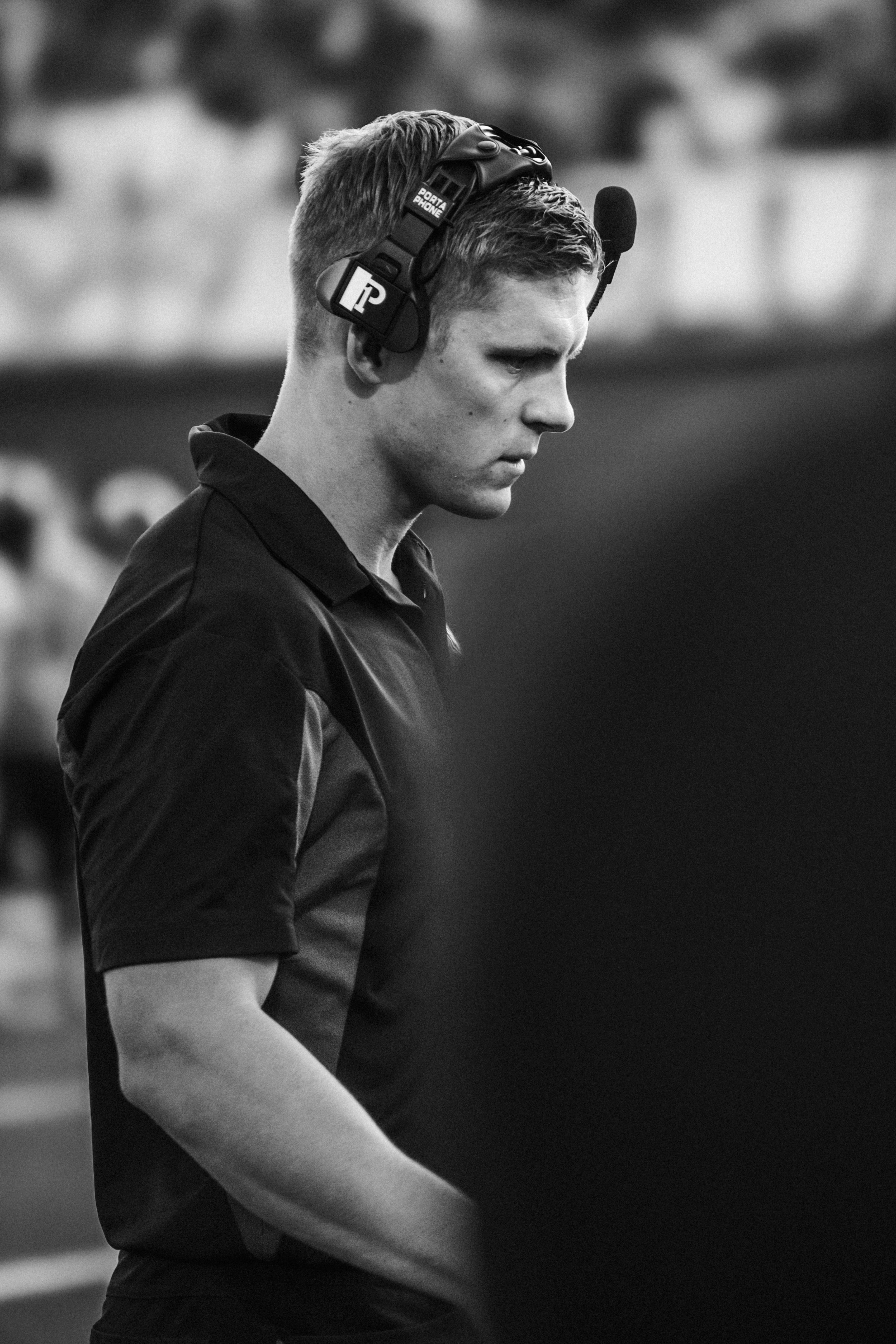 A focused football coach observes the game in a black and white portrait.