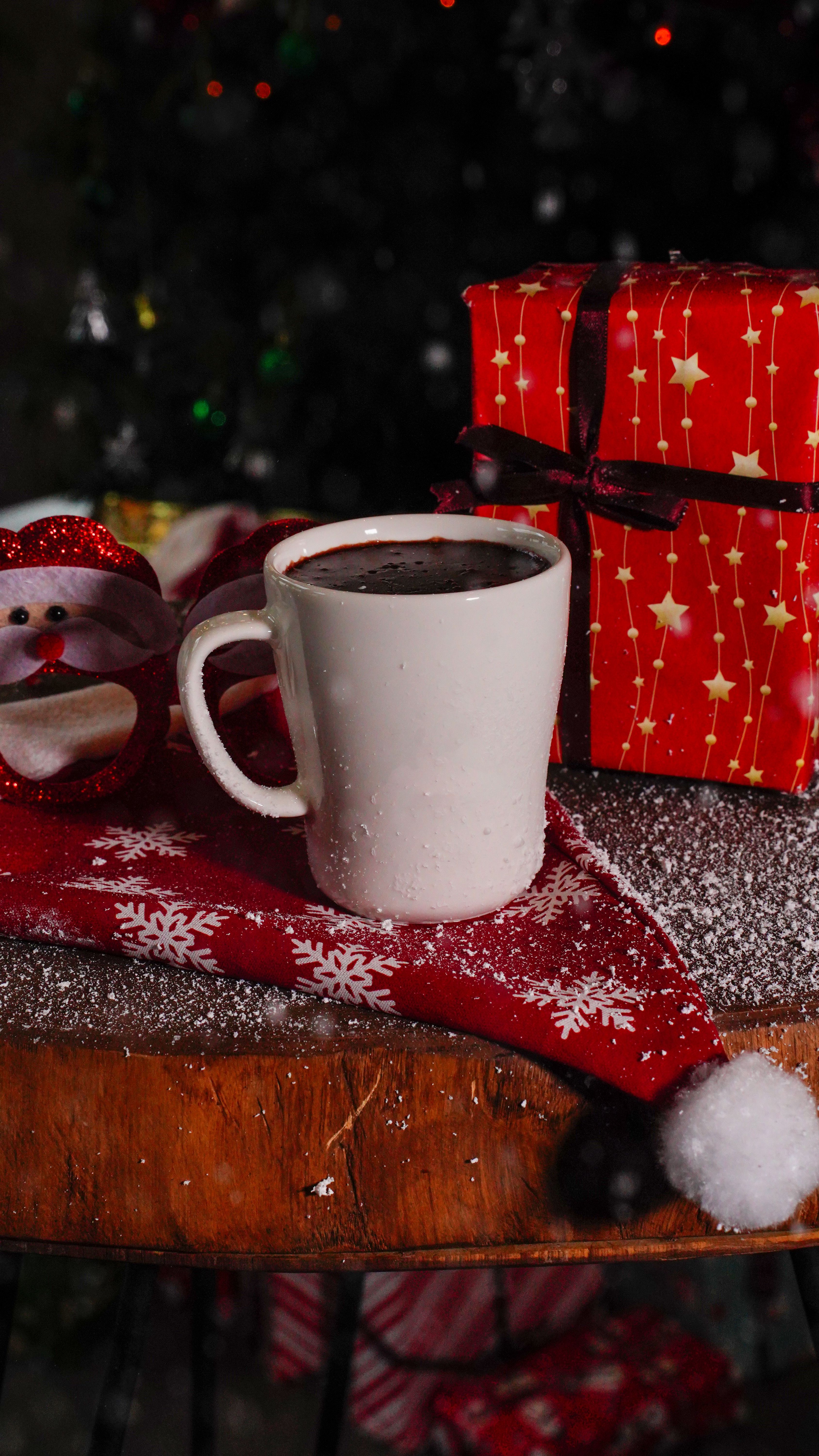 Cozy scene featuring hot chocolate, gift, and Santa ornament on a festive table setting.