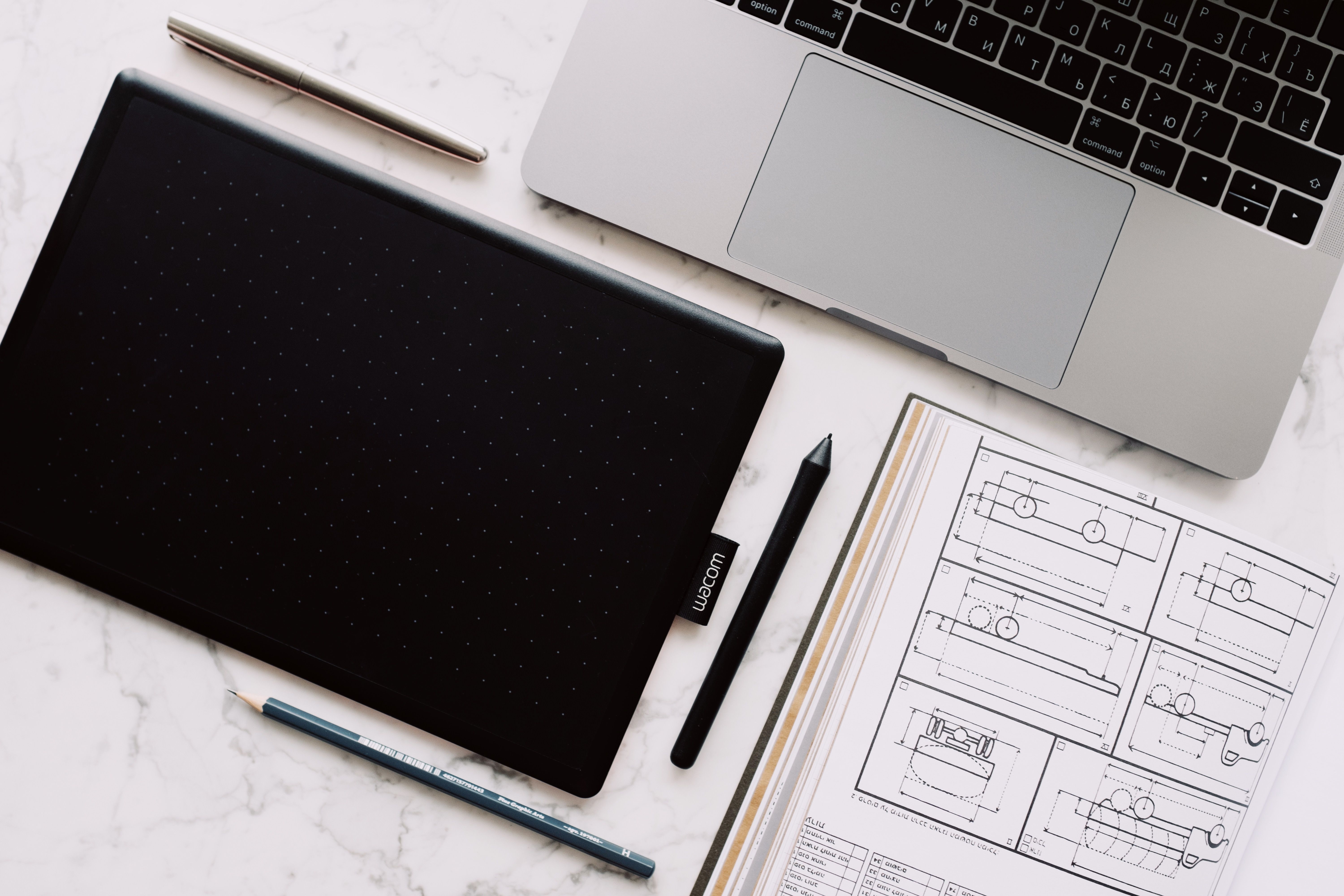 Top-down view of a desk setup including a laptop, drawing tablet, and design sketches.