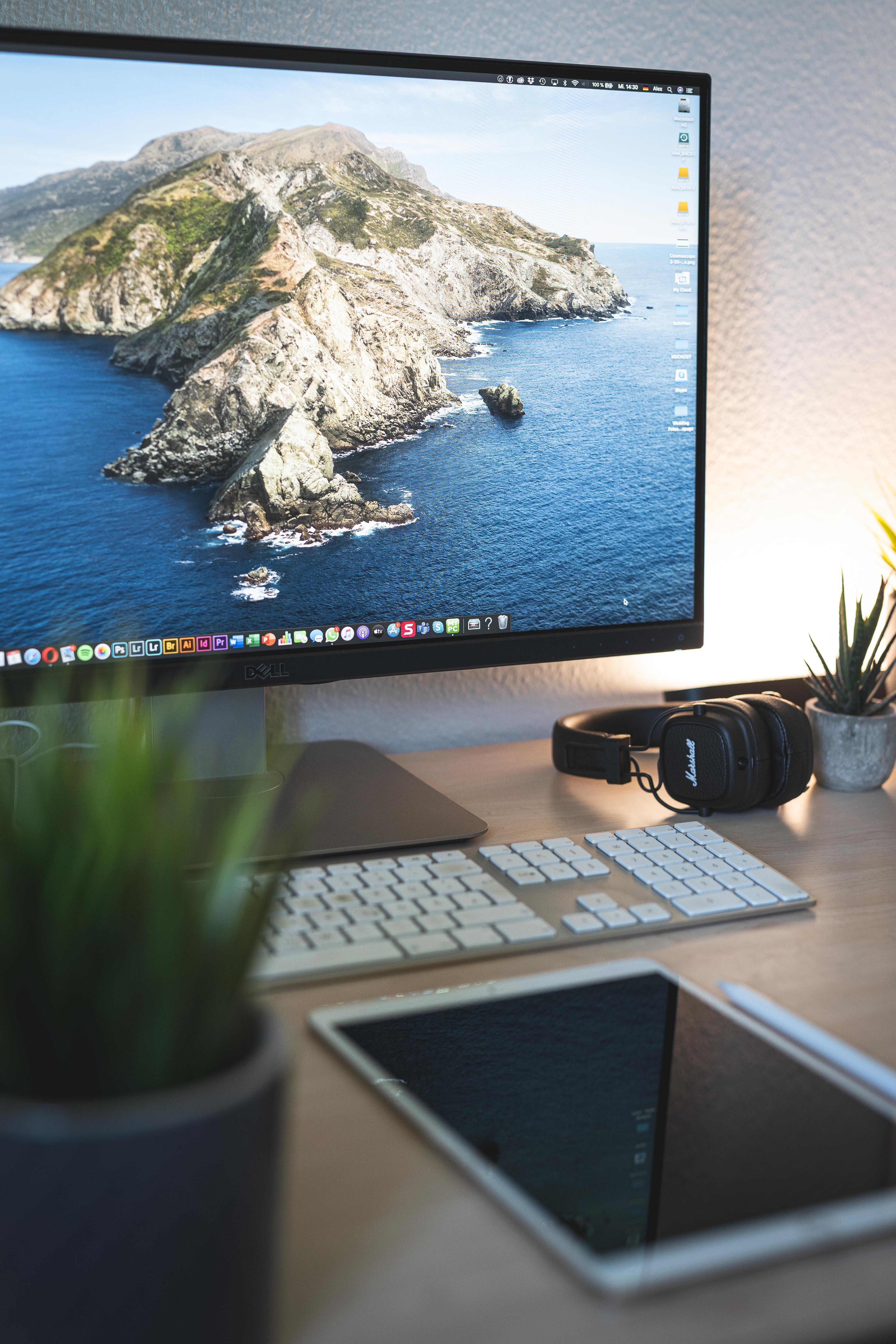 A sleek and organized desk setup featuring a computer monitor, keyboard, tablet, and headphones.