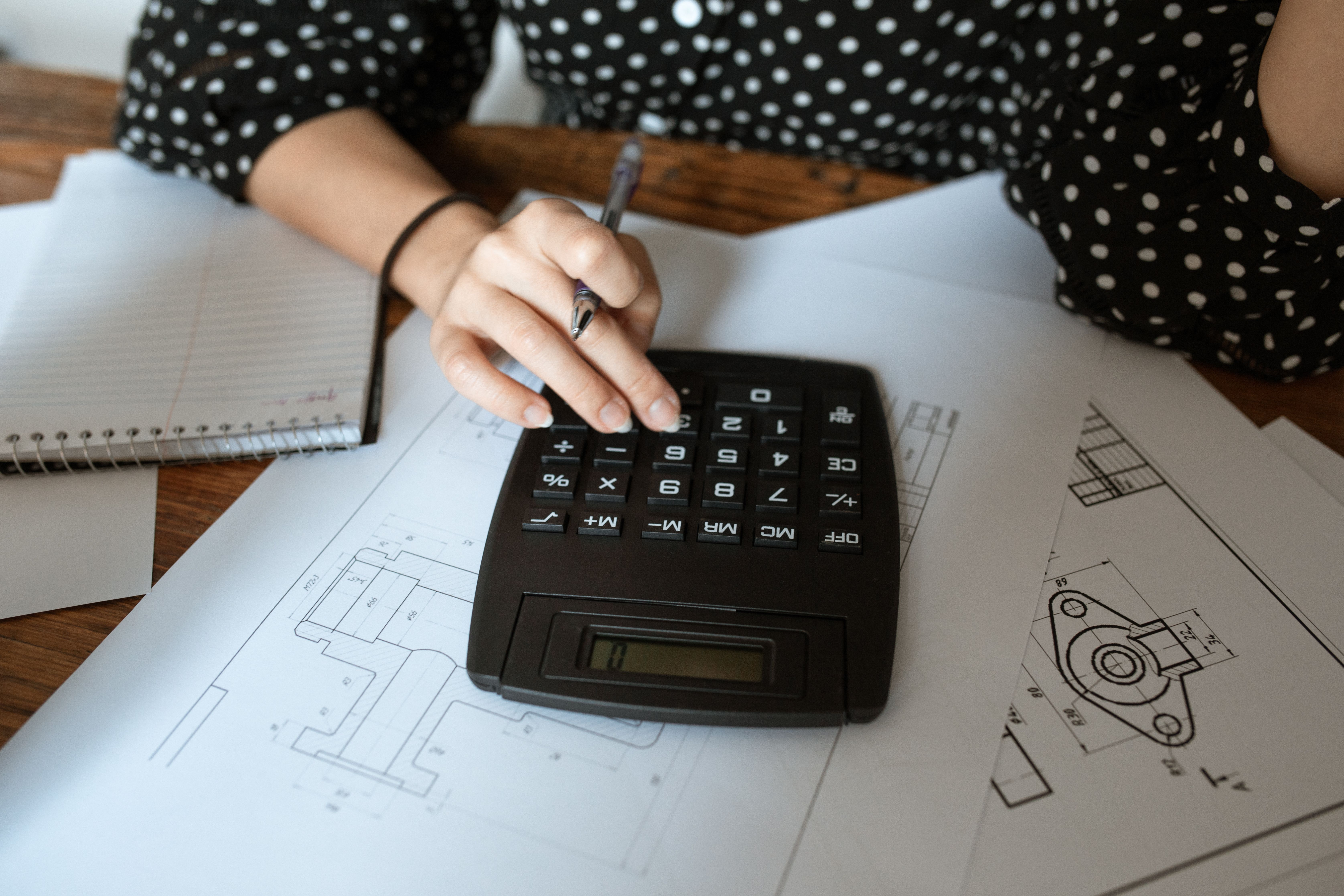 Close-up of an architect's hand using a calculator on technical drawings with a polka dot shirt.