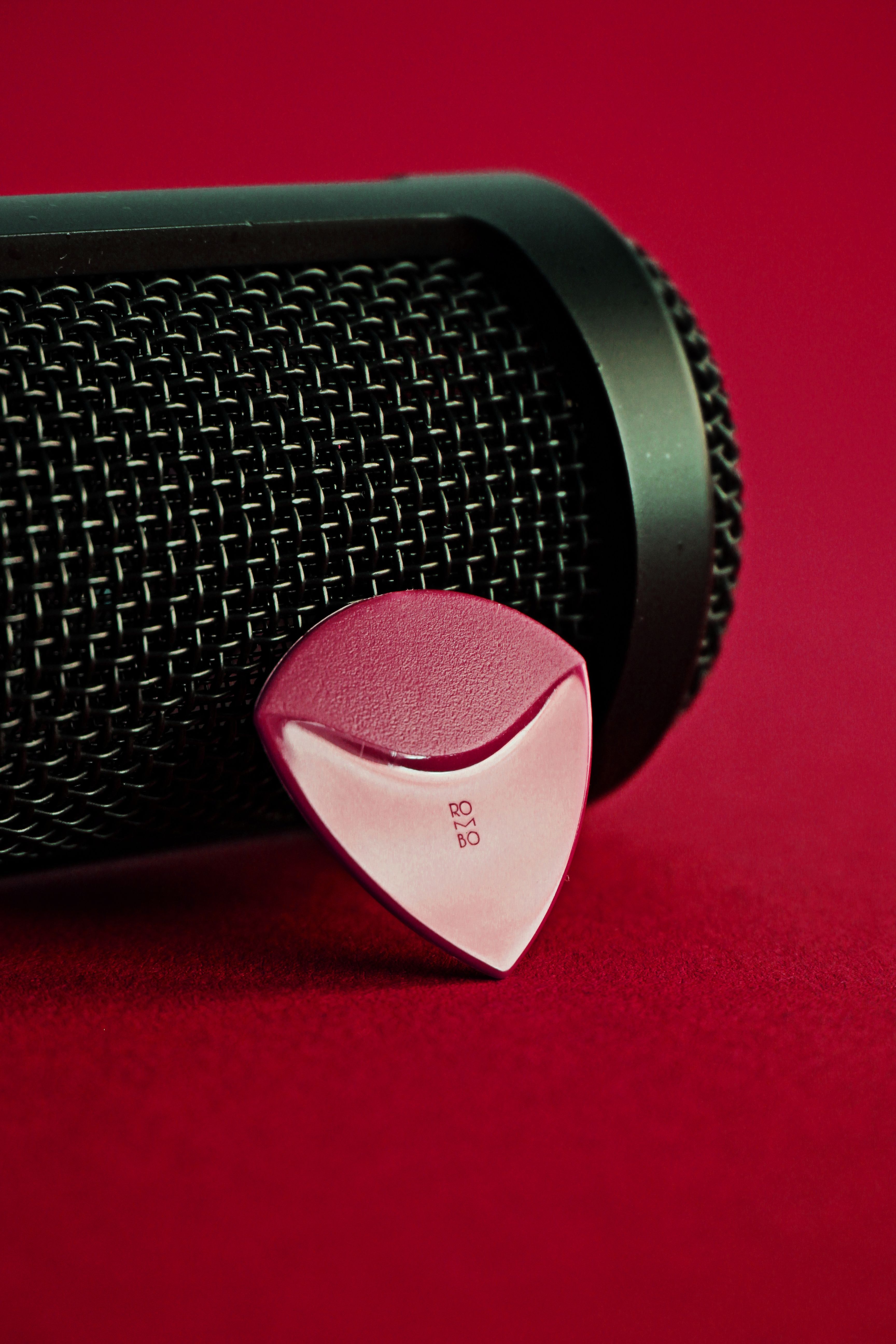 Close-up of a guitar pick resting against a microphone on a vibrant red surface.