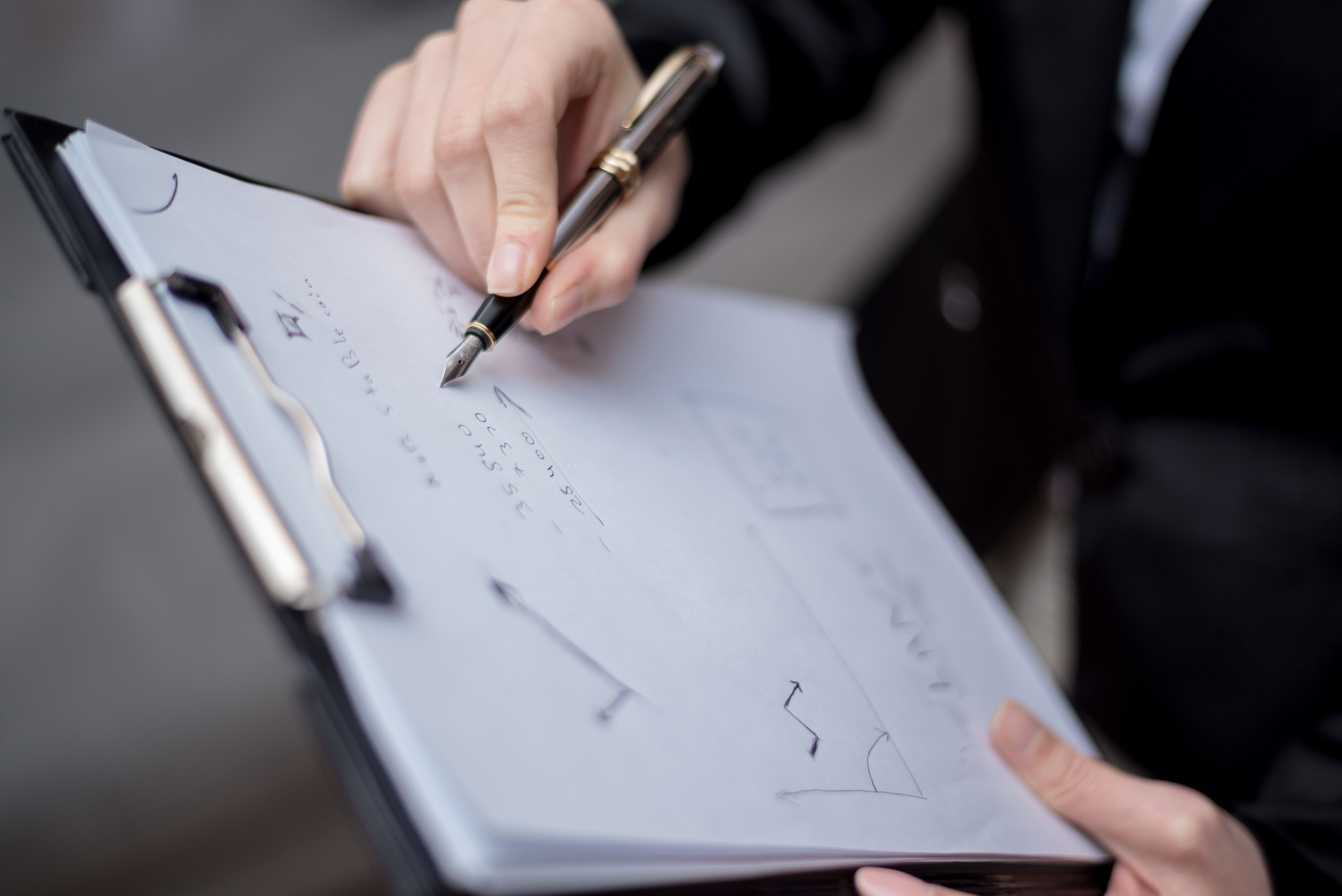 A person writing on a clipboard using a pen, focusing on the hand and paper.