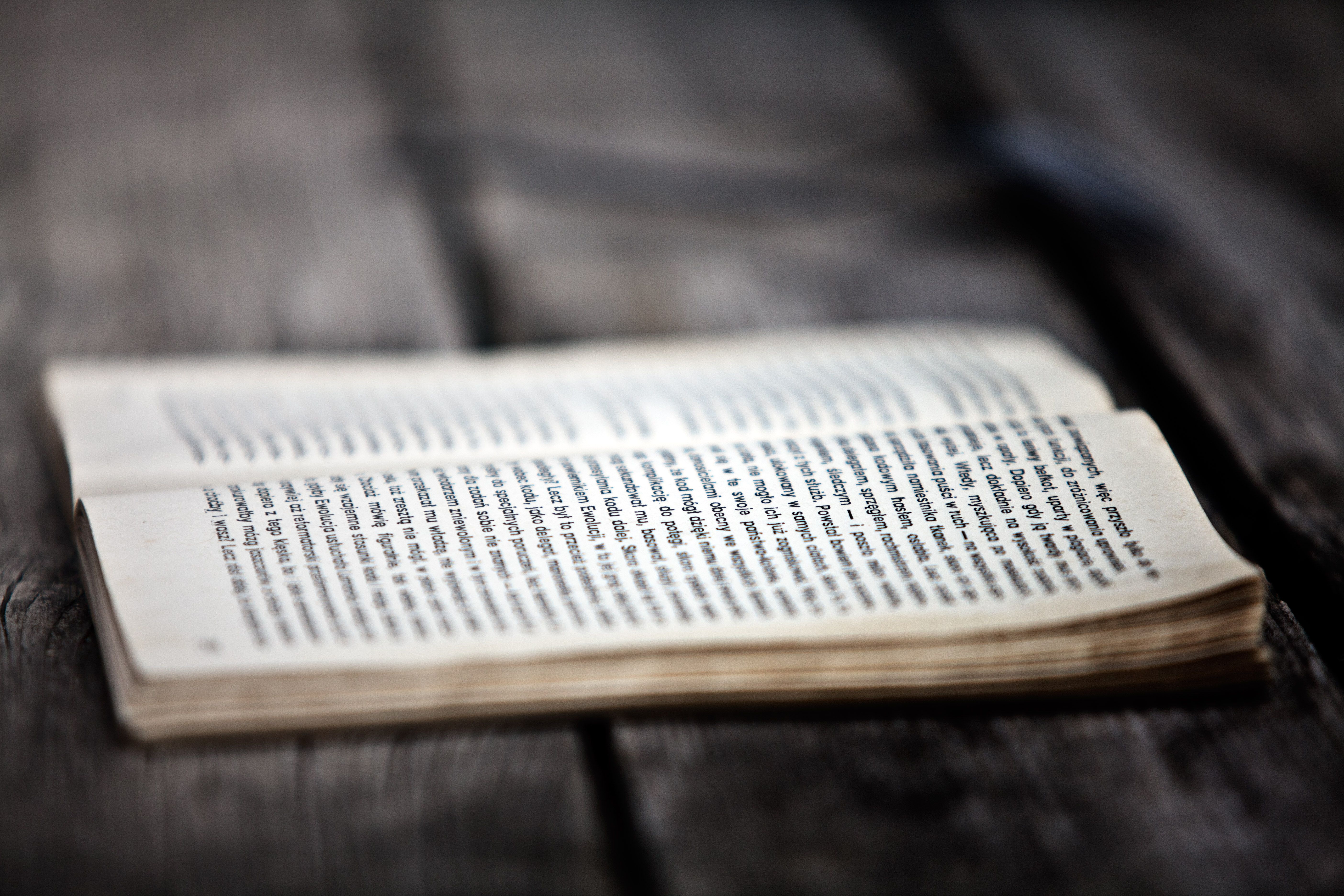 A close-up of an open book placed on a weathered wooden surface, with text in focus.