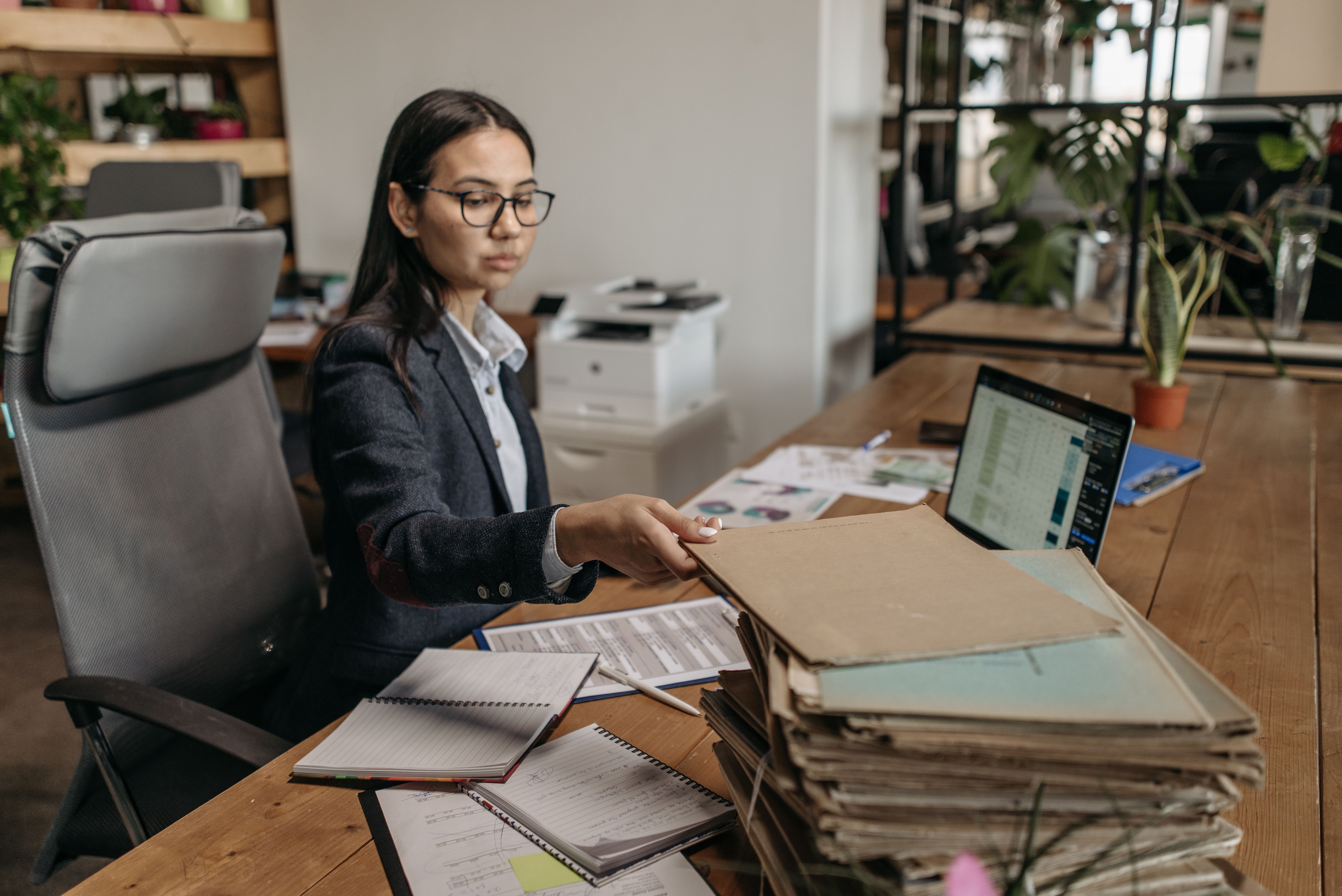 Businesswoman working at a wooden desk with documents and laptop in a modern office.